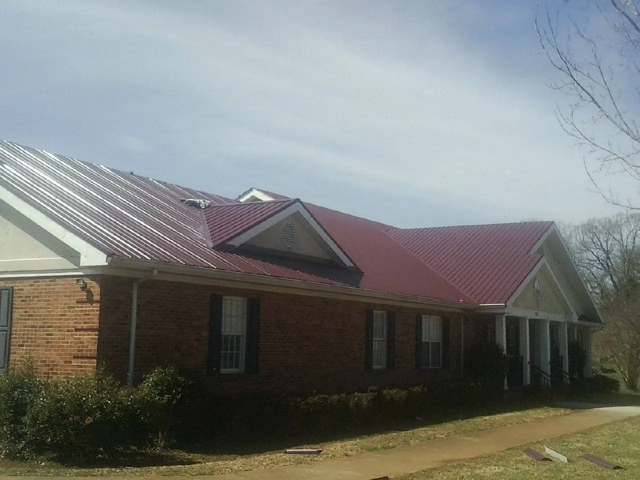 Red metal roof with gabled entries on a long brick building, from a Hail Damage Roof Repair job in Du Quoin