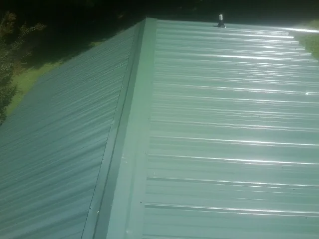 New green metal panels meeting at the ridge of a roof — Flat Roof Repair work by our crew in Du Quoin