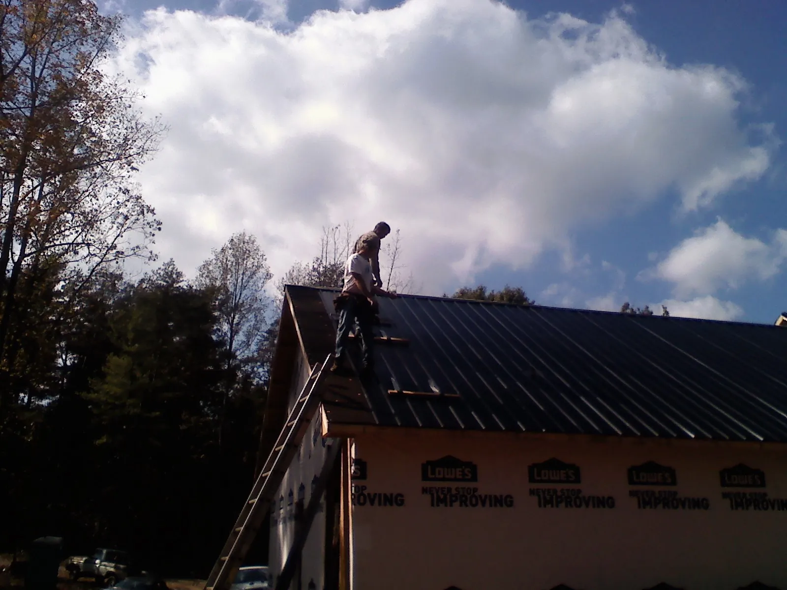 Roofer fastening dark metal panels high against a cloudy sky, from a Roof Inspection job in Du Quoin