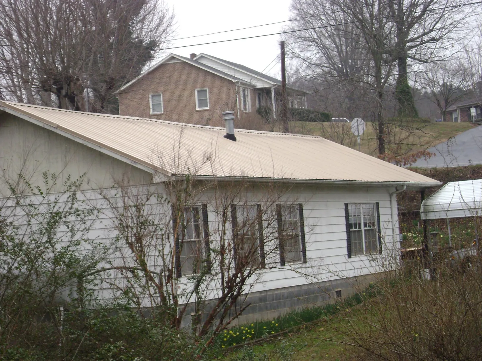 Tan metal roof on a white sided house set into a hillside — Commercial Roofing by Roofing Brothers in Du Quoin